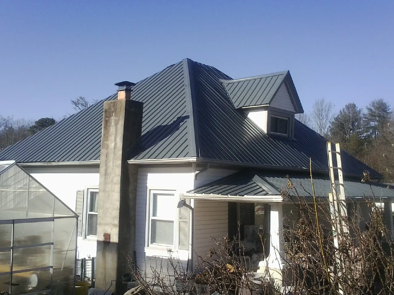 Dark blue standing seam metal roof on a white farmhouse with dormer — Slate & Tile Roof Repair by Roofing Brothers in Winnebago