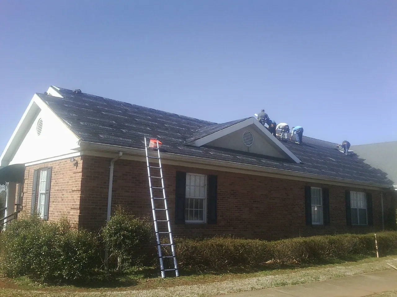 Crew tearing shingles off a brick ranch roof with a ladder set — Emergency Roof Repair work by our crew in Winnebago