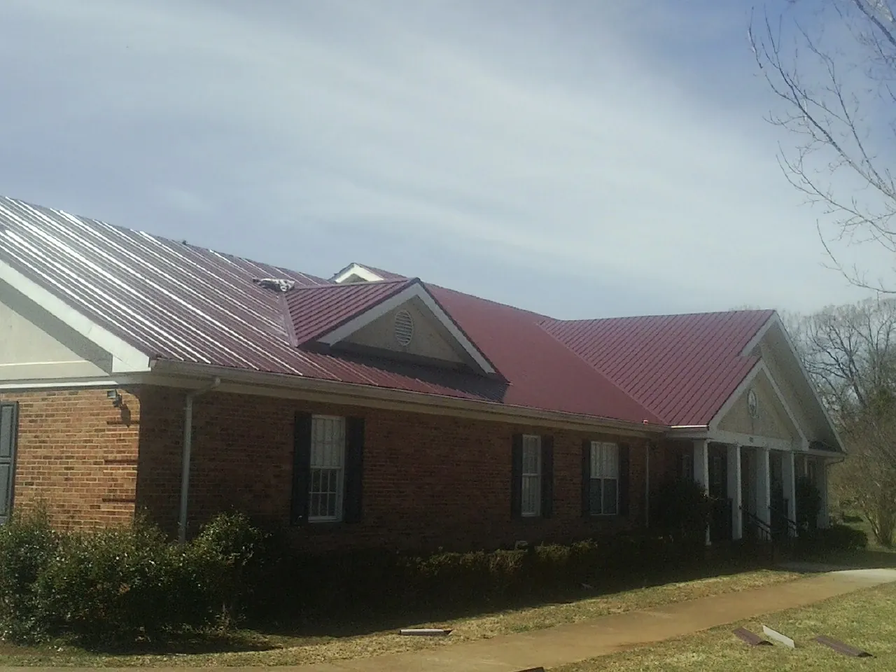 Red metal roof with gabled entries on a long brick building, from a Hail Damage Roof Repair job in Winnebago