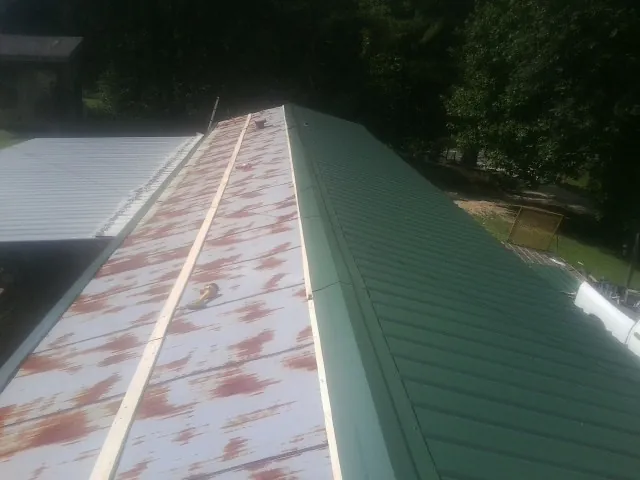 Old rusted panels beside newly installed green metal roofing — Wind Damage Roof Repair by Roofing Brothers in Winnebago
