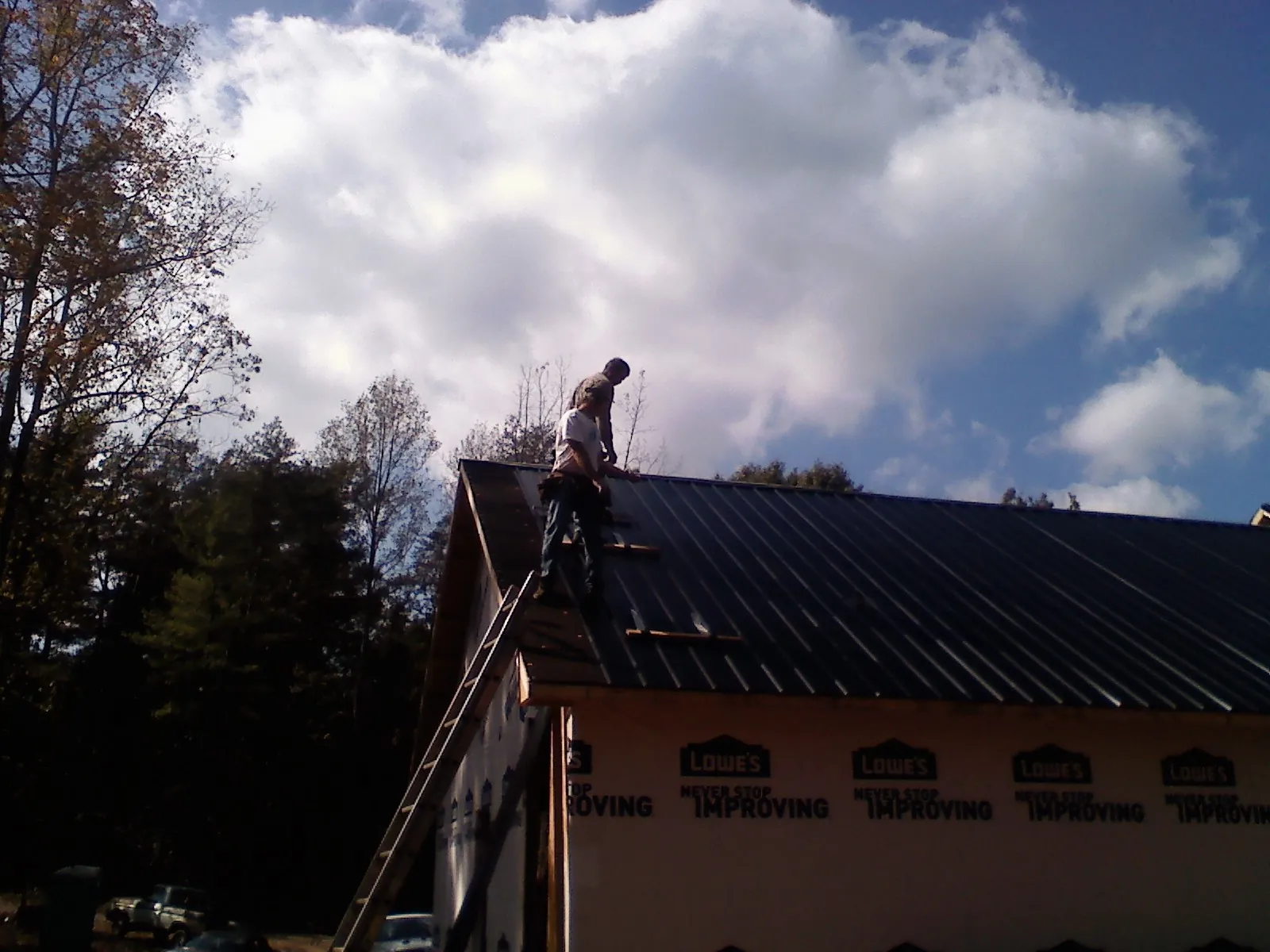 Roofer fastening dark metal panels high against a cloudy sky, from a Roof Inspection job in Winnebago