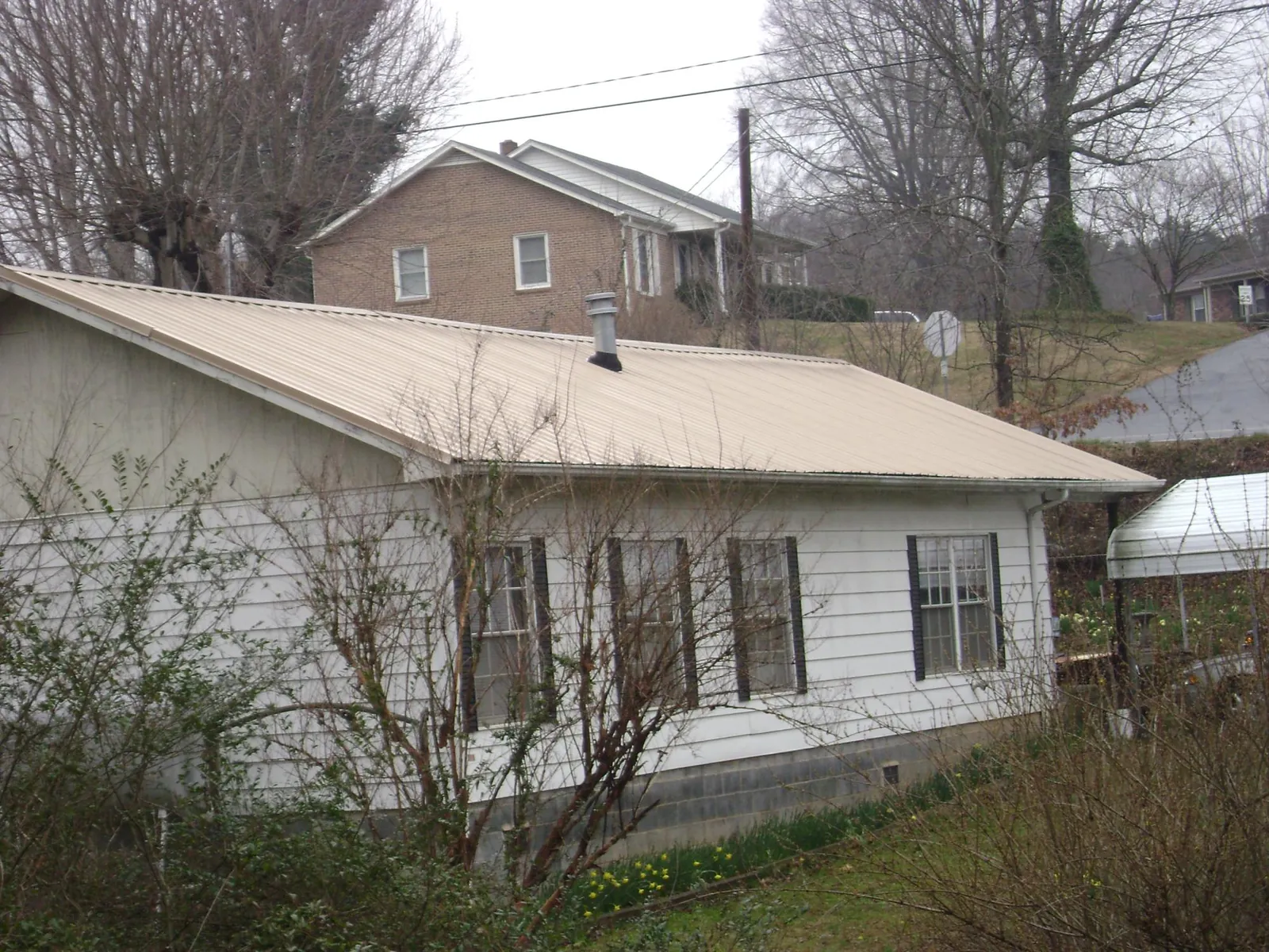 Tan metal roof on a white sided house set into a hillside — Commercial Roofing by Roofing Brothers in Winnebago