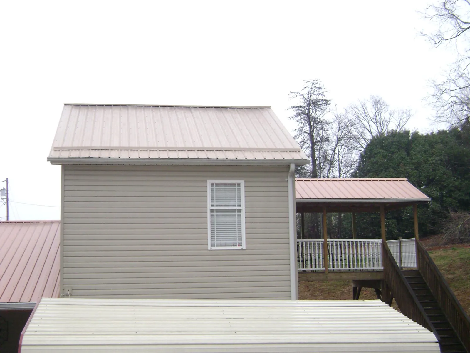 Tan metal roofs on a two story addition and attached porch, from a Roof Replacement job in Winnebago